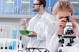 Teacher holding flask while little student looking in microscope