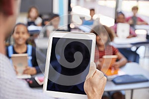 Teacher holding tablet in school class, over shoulder view