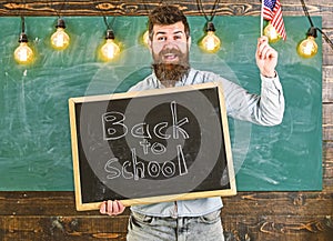 Teacher holds blackboard with written phrase back to school and flag of USA. Man with beard on smiling face welcomes to