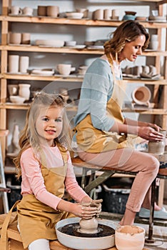 teacher and kid making ceramic pots on pottery wheels