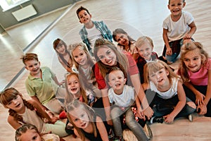 Teacher and kids. Happy female dance trainer with positive and cute children looking at camera and smiling while sitting