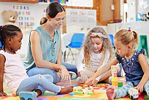 Teacher and kids looking happy while doing activity at kindergarten or pre-school. Smiling teacher sitting on a