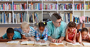 Teacher and kids lying on floor reading book in library