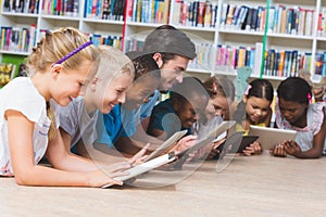 Teacher and kids lying on floor using digital tablet in library