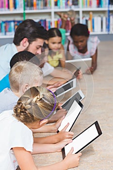 Teacher and kids lying on floor using digital tablet in library