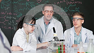 Teacher looking under microscope while test tube placed on table. Edification