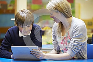 Teacher With Male Pupil Using Digital Tablet In Classroom