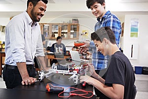 Teacher With Male Pupils Building Robotic Vehicle In Science Lesson