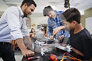 Teacher With Male Pupils Building Robotic Vehicle In Science Lesson