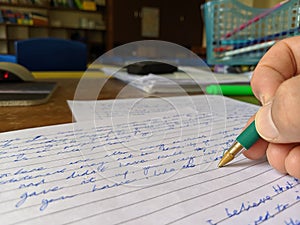 A teacher marking an exam paper at a desk with green pen in hand