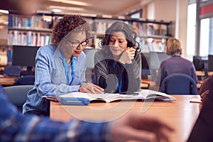 Teacher With Mature Female Adult Student Sitting At Table Working In College Library