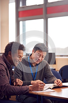 Teacher With Mature Male Adult Student Sitting At Table Working In College Library