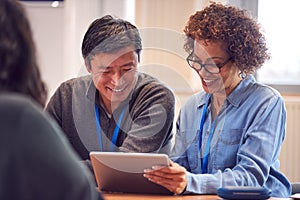 Teacher With Mature Male Adult Student Using Digital Tablet At Table Working In College Library