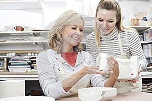 Teacher With Mature Woman Making Mug In Pottery Class