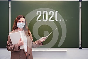 Teacher in a medical mask at the blackboard with an indeterminate year of the end of quarantine. Concept of problems at school