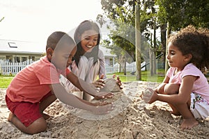 Teacher At Montessori School Playing With Children In Sand Pit