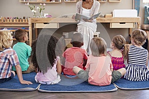 Teacher At Montessori School Reading To Children At Story Time