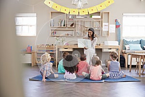 Teacher At Montessori School Reading To Children At Story Time