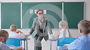 Teacher near blackboard leads lesson, schoolchildren listen to pedagogue and raises hands knowing the right answer get
