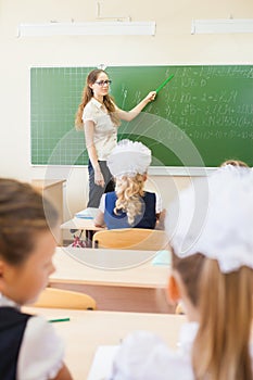 Teacher near blackboard teaching children math or geometry, holding pointer.