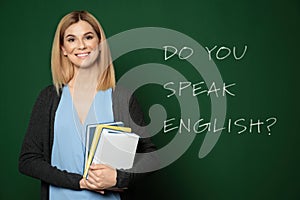 Teacher near green chalkboard with text Do You Speak English