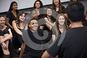 Teacher At Performing Arts School Talking To Students Sitting On Floor In Rehearsal Studio
