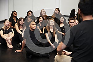 Teacher At Performing Arts School Talking To Students Sitting On Floor In Rehearsal Studio