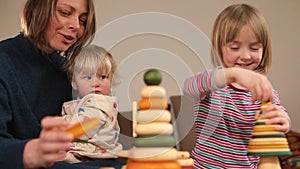 Teacher plays pyramids with children on table. She holds the baby in her arms.