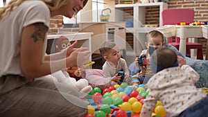 Teacher and preschool students playing with balls and cars sitting on floor at kindergarten