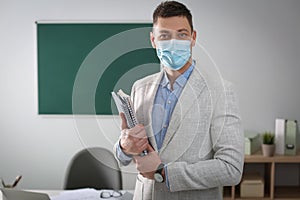 Teacher with protective mask and copybooks in classroom. Reopening after Covid-19 quarantine