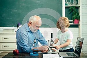 Teacher and pupil learning together in school. Happy cute Grandson and Grandfather sitting at a desk indoors. Elementary