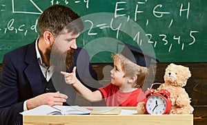 Teacher and pupil in mortarboard, chalkboard on background. Naughty child concept. Kid cheerful distracting while