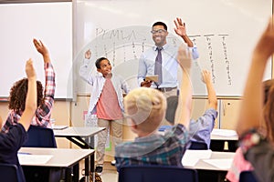 Teacher and pupil with raised hands at front of school class