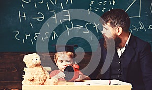 Teacher and pupil sitting in the classroom. Adult man in smart suit is looking to the side while kid is playing with