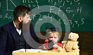 Teacher and pupil sitting in the classroom. Adult man in smart suit is looking to the side while kid is playing with