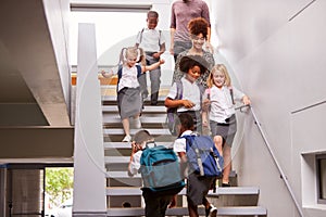 Teacher And Pupils Walking Down Stairs In Busy Elementary School Corridor