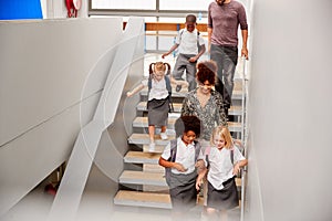 Teacher And Pupils Walking Down Stairs In Busy Elementary School Corridor