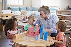 Teacher And Pupils Working At Tables In Montessori School