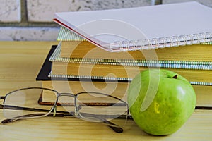 Teacher's Day concept and back to school, green Apple, book, laptop, reading glasses and pen on wooden table, sunlight