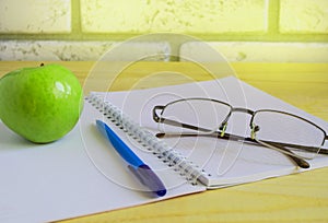 Teacher's Day concept and back to school, green Apple, book, laptop, reading glasses and pen on wooden table, sunlight