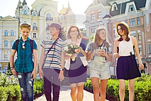 Teacher`s Day, outdoor portrait of happy middle aged female high school teacher with bouquet of flowers and group students.