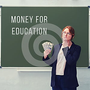 A teacher in a school class holds in his hands money in dollars. The text on the school board