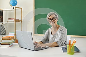 Teacher school university online. Woman senior teacher speaks with students has web chat using laptop computer sitting