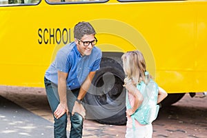 Teacher and schoolgirl interacting in front of school bus