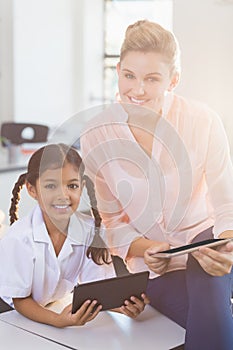 Teacher and schoolgirl using digital tablet in classroom