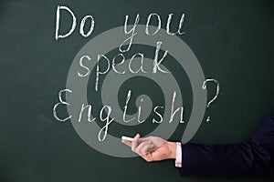 Teacher showing words Do You Speak English? written on green chalkboard, closeup