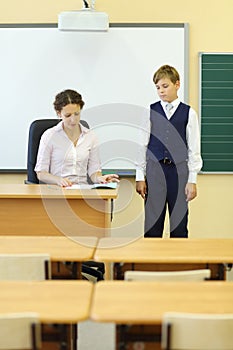 Teacher sits at table and checks exercise book and photo