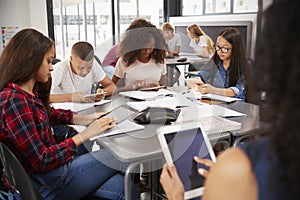 Teacher sitting with high school students using tablets