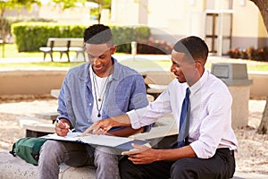 Teacher Sitting Outdoors Helping Male Student With Work