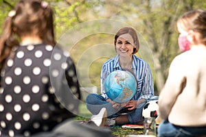 Teacher with small children sitting outdoors in city park, learning group education concept.